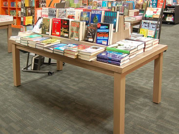 Store displays a long table with tiers displaying a variety of books - Different Angle