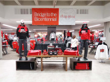 Store displays mannequins on pedestals wearing school colors. Clothing racks and store view